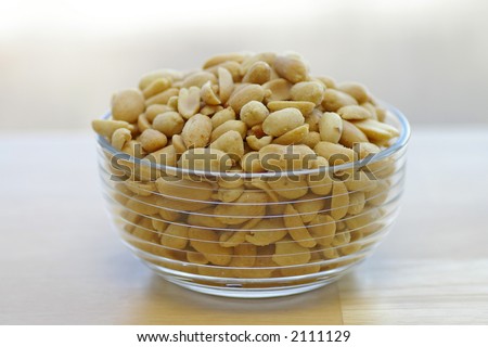 Roasted, shelled, and salted peanuts in a glass bowl on a butcher-block tabletop