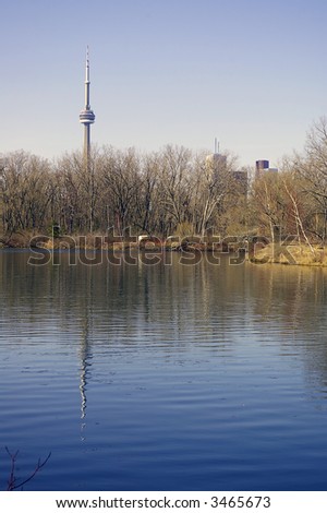 A view of the CN Tower and Roger\'s Centre (formerly Skydome) from Centre Inland.  Skyline view is reflected in the water, and budding trees visible along right shoreline.