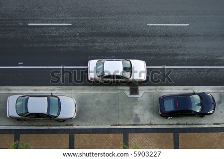 A silver car stopped on the road between two parked cars preparing to parallel park against curb.