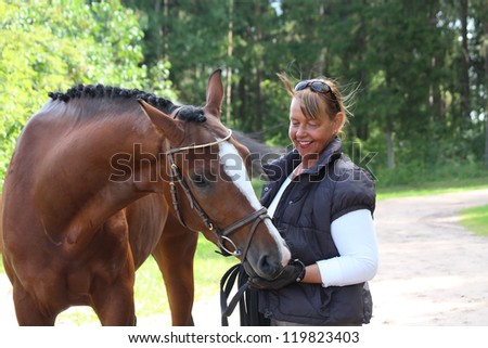 Happy smiling elderly woman and brown horse portrait in the forest