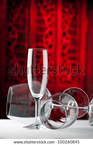 Champagne wine glass standing on a table with red wine glass and white wine glass lied down in front of a beautiful dark red background
