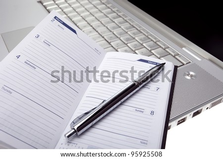 Silver lap top with opened pocket planner and silver pen close up