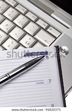 Silver lap top with pocket planner and silver pen close up