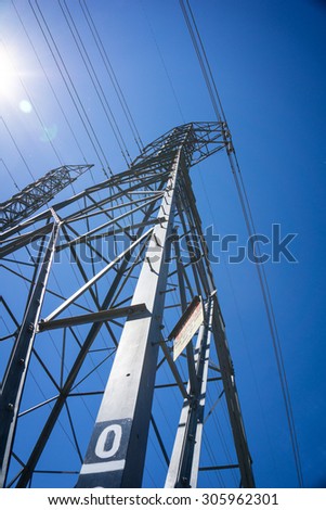 Line of massive metal electric tower structure holding up wires high above the ground.