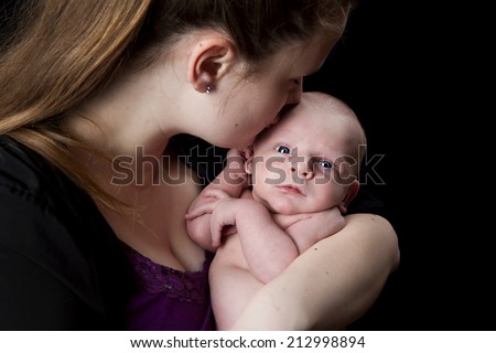 A new mother kissing her infant son.  Isolated on black.