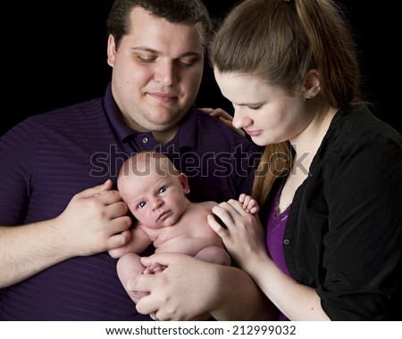 New parents holding their infant son.  Isolated on black.