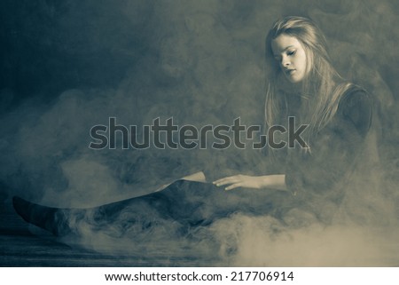 Beautiful young woman in a fog.  Low lighting and fog to give a moody feel to the image. Editing includes some noise for effect.