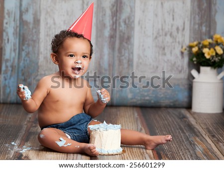 Adorable baby boy wearing a red party hat and eating a small birthday cake.