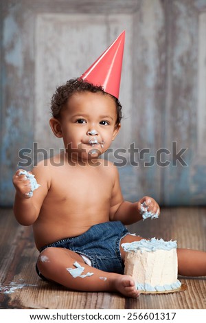 Adorable baby boy wearing a party hat and eating a small birthday cake.