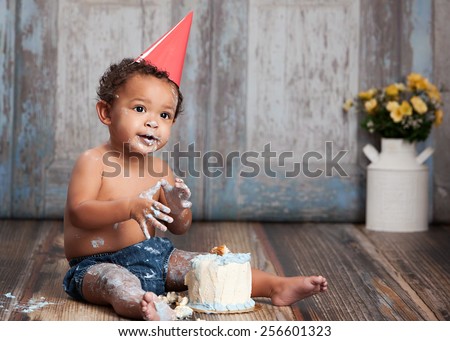 Adorable baby boy wearing a red party hat and eating a small birthday cake.