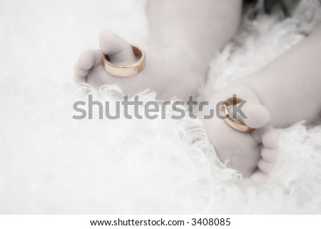 An infant\'s feet with it\'s parent\'s wedding rings on each big toe.  Black and white with gold rings.