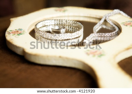 Diamond jewelry on the glass of a hand mirror.  Shallow depth of field with focus on diamond of ring.