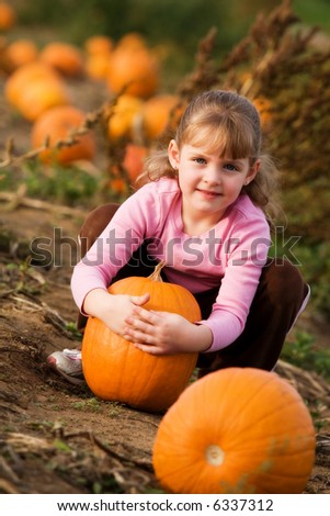 Happy little girl hugging the pumpkin she\'s selected from a pumpkin patch.
