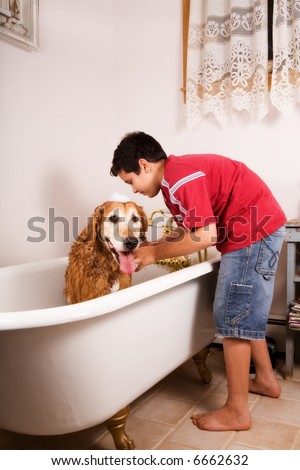 Preteen boy bathing his golden retriever in his home's bathtub.