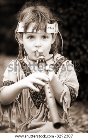 Little girl dressed as a Native American playing a wooden flute.  In sepia tone.