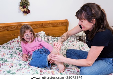 A mother and daughter playing tickle on a big bed.