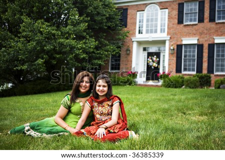 Indian mother and daughter, dressed in saris on the front lawn of their home.