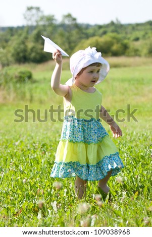 Happy little girl playing with a paper plane in summer field