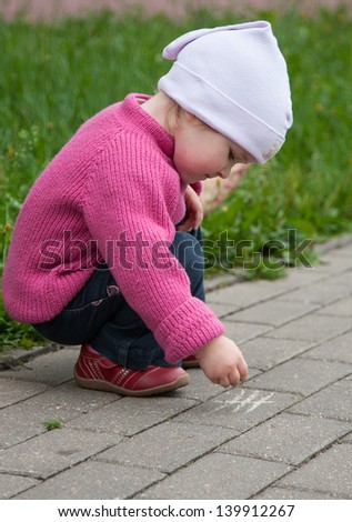 Little girl drawing with a chalk on pavement