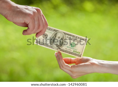 Hand proposing dollar banknote to the other hand, light green background