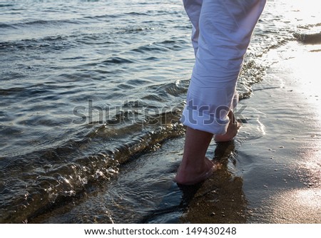 Woman legs walking along the sea coast at sunset