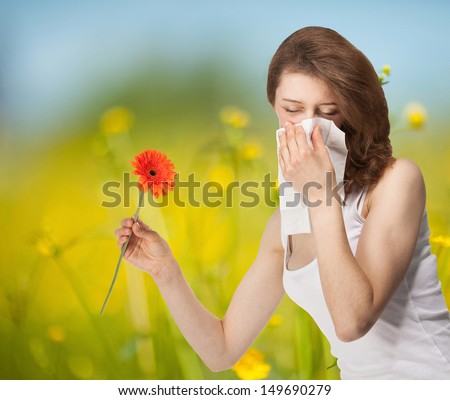 Young woman having allergy staying outdoors in a summer meadow with red herber