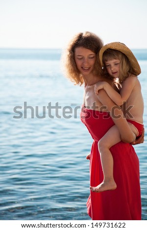 Happy mother and daughter walking near the seashore in limpid water
