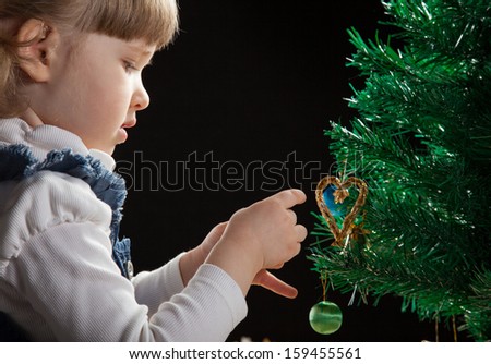 Beautiful little girl decorates the Christmas tree, black background