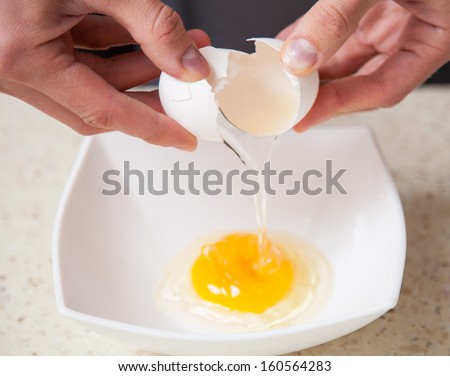 Female hands holding cracked egg over a white bowl