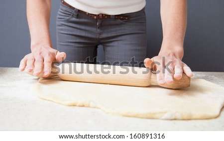 Housewife  flattening a dough with a rolling pin on dark background