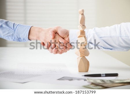 Business people shake hands near built wooden tower (Japanese game tumi-ishi), illustrating concept of business success, cooperation, achievement and self-control