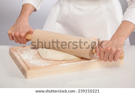 Unrecognizable cook\'s hands rolling out dough on wooden board, gray background