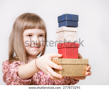 Pretty little girl holding gift boxes on neutral background