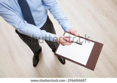Businessman holding a clipboard with empty sheet of paper and proposing a pen, white background
