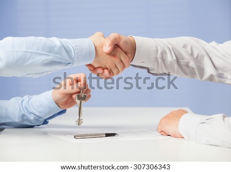 Businessman passing keys to his partner and shaking his hand, blue background