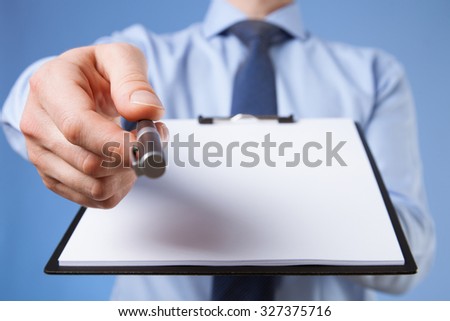 Businessman holding a clipboard with empty sheet of paper and proposing a pen, blue background