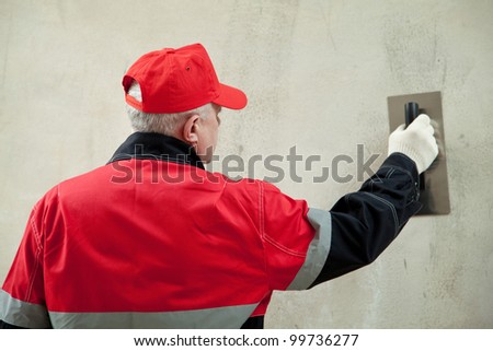 Back view of a plasterer in uniform working with float against the wall