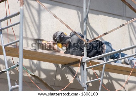 Workman Laying on Scaffolding Grinding a Concrete Wall