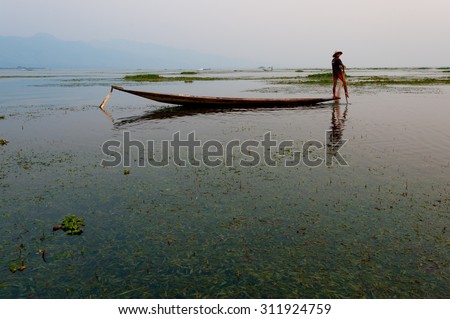 INLE LAKE, MYANMAR - FEBRUARY 15: Unidentified man rowing a wooden boat in Inle Lake with its leg-rowing and fishing. Intha people is a major tourist destination on Feb 15, 2011 in Inle lake, Myanmar.