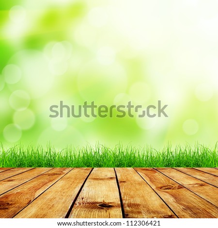 Fresh spring green grass with green bokeh and sunlight and wood floor. Natural background