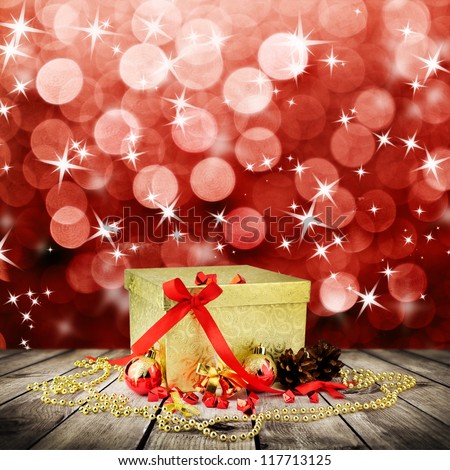 Golden christmas gift box with christmas balls on wooden planks over red blured background
