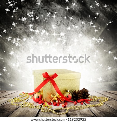 Golden christmas gift box with christmas balls on wood planks over dark background with light rays with stars