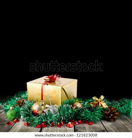 Golden christmas gift box with christmas balls on wood planks over black background