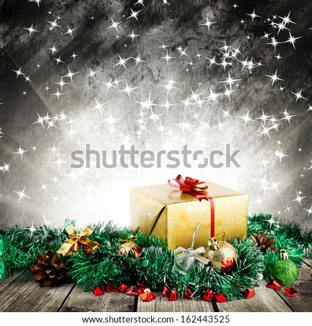 Golden christmas gift box with christmas balls on wood planks over dark background with light