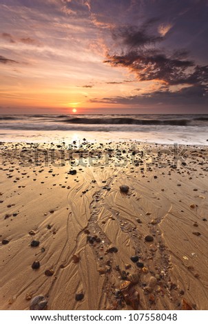 Water flows across the beach into the sea creating lines in the sand as the sun appears above the horizon