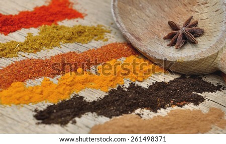 bands of different spices powder and anise in  spoon on wooden  background