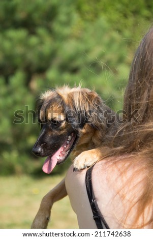 Young woman is holding a dog. Woman is turned back to the camera and the dog is looking over her shoulder to the side. Shooting outdoors.
