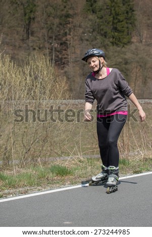 Active middle aged woman is skating on rollerblades outdoors. All potential trademarks are removed.