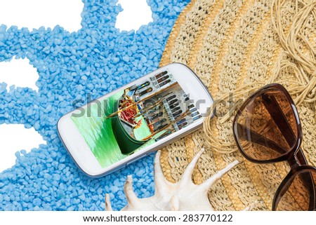 Straw hat, sunglasses and a seashell are lying on a little blue stones isolated on the white. Display of the cell phone contains photo of gondola in Venice.All potential trademarks are removed.