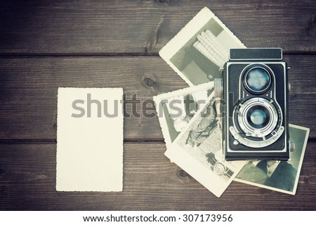 Vintage photo of the old blank photo is lying on a wooden desk  in the left  edge of the photo. On the right side of the photo is laying old camera on an old photos. All  trademarks are removed.